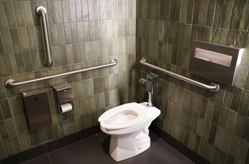 Accessible restroom, featuring a modern, muted green tile wall and stainless steel grab bars.