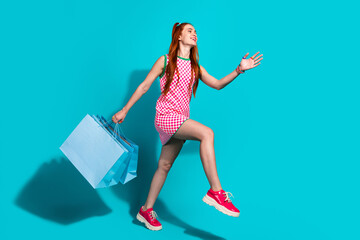 Cheerful young woman enthusiastically carries shopping bags in a vibrant turquoise background...