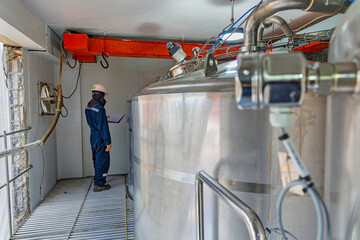 Male work inspection process stainless steel tanks and pipe with pressure meter in equipment tank facility for drink cellar at the with vertical stainless