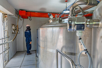 Male work inspection process stainless steel tanks and pipe with pressure meter in equipment tank facility for drink cellar at the with vertical stainless
