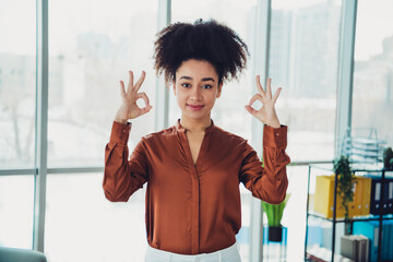 Young businesswoman demonstrating confidence while holding hand gestures in brightly lit modern...
