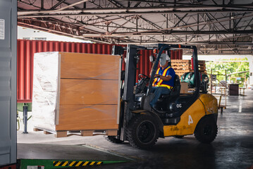 Factory Worker Driving Forklift in Warehouse with Safety Helmet Moving Carton Pallets to Container for Export Delivery