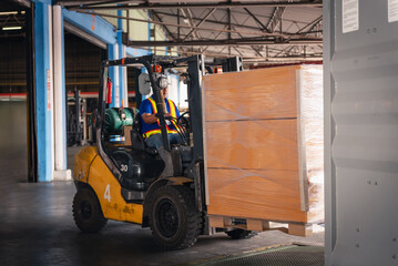 Factory Worker Driving Forklift in Warehouse with Safety Helmet Moving Carton Pallets to Container for Export Delivery