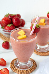 Strawberry mango smoothie in a glass on white kitchen table. Healthy summer blended drink.