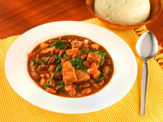 BeansStewBeef-Mozamb, Bohnensuppe mit Beef auf weissem Teller auf gelbem Tischset, afrikanisches essen, bohneneintopf,