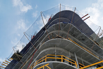 Modern concrete building rises under a clear sky, safety nets and scaffolding showing progress and precision of urban construction.
