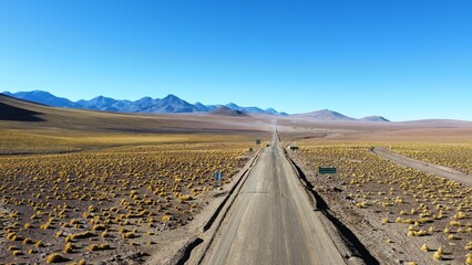 imagem aérea da rota do sol no chile, em dia claro e ensolarado. estrada serpenteia entre montanhas e vales secos, com céu azul e paisagem típica da cordilheira dos andes © RNL Fotografia