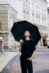 Beautiful girl standing under a black umbrella in the rain