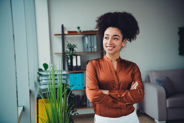 Confident businesswoman with curly black hair standing in a modern office with plants and bright...
