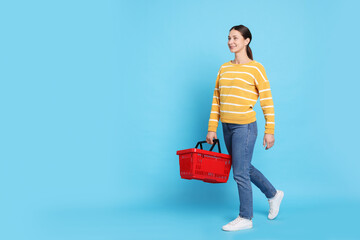 Smiling woman with shopping basket on light blue background. Space for text