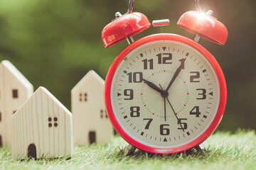 time alarm clock with miniature wooden home model outdoor for times to move or buy new home concept