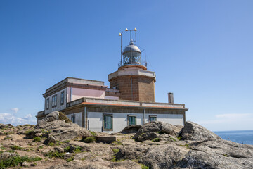 Finisterre Lighthouse on a rocky cliff in Galicia, Spain, overlooking the Atlantic Ocean at sunset. Built in 1853, it marks the legendary end of the world.