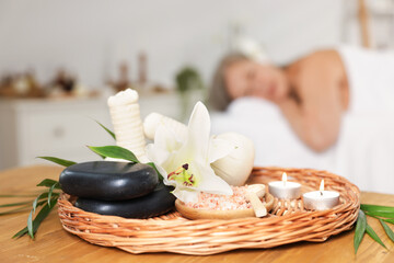 Senior woman relaxing on massage couch indoors, selective focus. Different spa products and lily flower on table