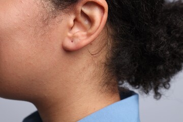 Young woman with pierced ear on light grey background, closeup