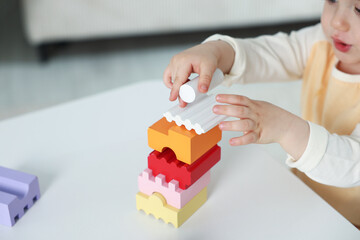 Cute little child playing with building bricks at white table indoors, closeup