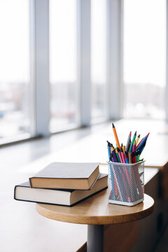 Books and pencils on a round wooden table by window