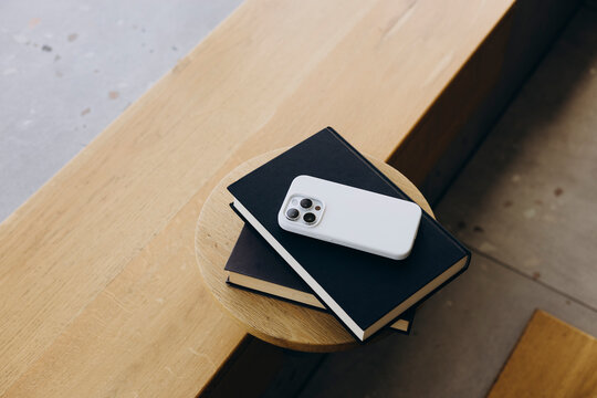 Smartphone resting on black books on wooden table