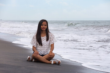 Fototapeta premium young woman sitting on wet black sand beach near waves