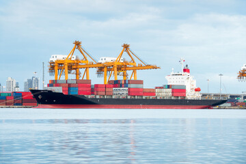 Fototapeta premium Cargo vessel loaded with colorful shipping containers sails through calm waters near busy port. The scene symbolizes global trade, international logistics, and maritime transportation.
