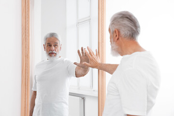 Obraz premium Handsome senior man looking at himself in mirror indoors