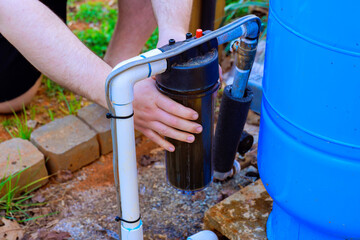 Person changing water filter connected to rainwater collection system outdoors in garden setting.
