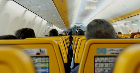 Passengers arranged on yellow seats in light comfortable salon of airplane. Tourists sit on chairs...