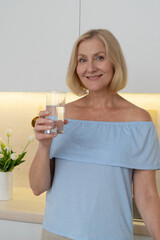 A smiling woman holds a refreshing glass of water surrounded by fresh vegetables in a stylish...