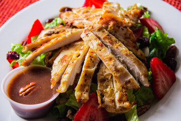 A tantalizing grilled chicken salad topped with fresh strawberries and a side of rich dressing, embodying a healthy and delicious option for any mealtime or gathering.