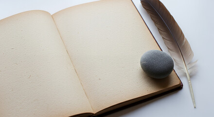 Open vintage book with feather quill and stone on white background for intentional living concept