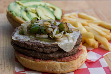 A vibrant burger featuring fresh avocado slices, melted cheese, grilled onions, and beans, complemented by a side of crispy fries for a tasty meal packed with flavor.