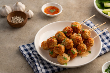 Air fryer cooked Thai Pork meatballs on skewers on white plate with chilli sauce.