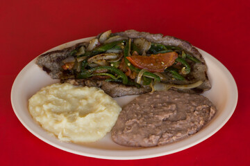 This image highlights a grilled steak loaded with onions, served alongside creamy mashed potatoes and refried beans, creating a delightful meal that's visually inviting.