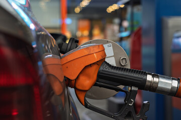 Bright orange fuel nozzle is inserted into a car's gas tank, reflecting the routine moment of refueling at a modern gas station.