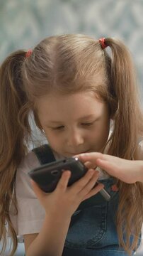 little children of different ages, show each other tongue, girl with pigtails holds smartphone, boy is blond - bottle with dummy, they sit on floor in living room, brother and sister smiling close up