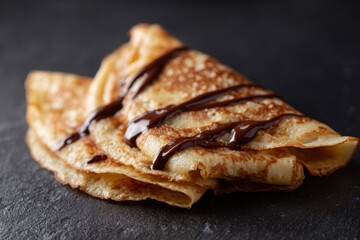 Delicious crepes drizzled with chocolate on dark background