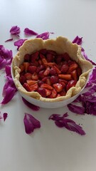 A cozy homemade dessert setting with fresh cookies and an unbaked strawberry pie, beautifully styled with purple flower petals and a white vase of peonies.