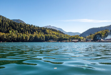 Lake Ritsa, framed by majestic mountain peaks, reflects the tranquility of its turquoise surface. The slopes of the surrounding mountains are covered with lush greenery.