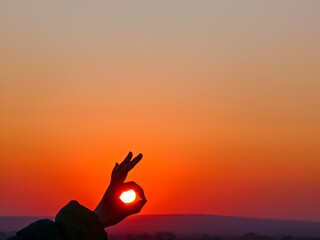 The setting sun is perfectly framed by a hand in the classic 'okay' gesture.