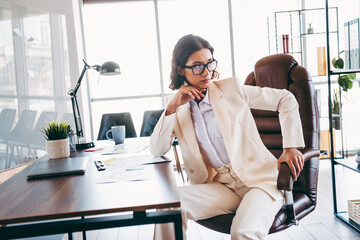 Confident businesswoman in a stylish white suit seated in a modern corporate office environment...