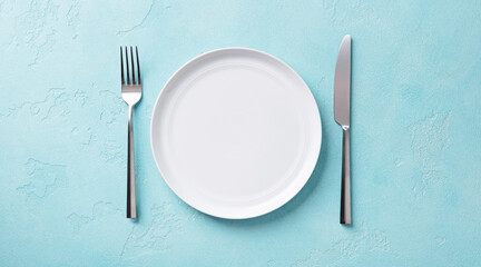 Empty white plate with fork and knife on a blue stone background. Flat lay. Copy space. Top view.