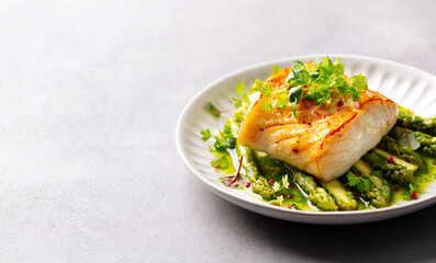 Roasted cod with asparagus and on plate. Grey background. Close up. Copy space.