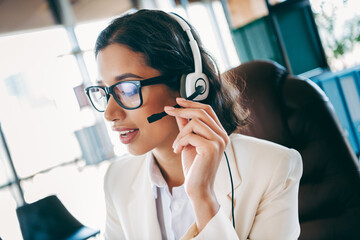 Confident businesswoman with headset working in a modern office environment, reflecting...