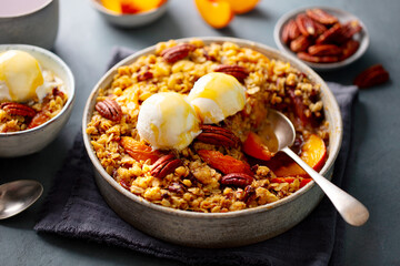 Healthy breakfast. Peach crumble cake with ice cream and pecan nuts in bowl. Grey background. Close up.