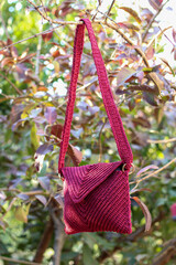 Crochet red bag hanging from a branch of a tree with red leaves. Hand made. 