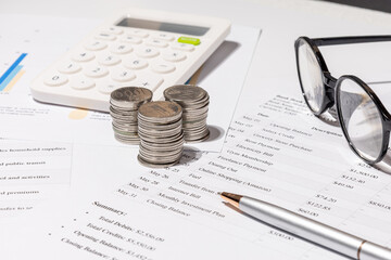 Detailed Family Expenses Breakdown Sheet with Coins and Calculator on the Desk