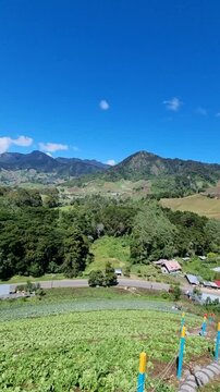Wide landscape showing cultivated hills and a mountain village under a bright blue sky with scattered clouds, Cerr punta Boquete Panama.