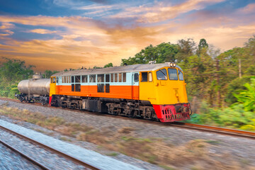 Yellow locomotive diesel train moving rushes with a trailer barrels bulk cargo fuel oil