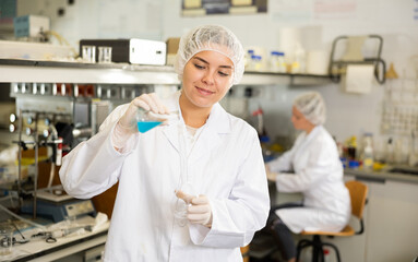 Professional female chemist working in laboratory, analyzing liquid samples in test flasks