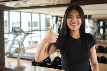 portrait of a young woman giving thumbs up in gym while smiling
