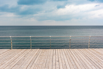 Empty seaside promenade with wooden decking and metal handrails on a cloudy day